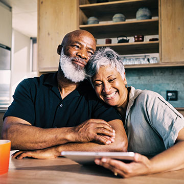 A married couple lean on each other as they laugh about what they saw on their tablet device. Links to Gifts of Real Estate A married couple lean on each other as they laugh about what they saw on their tablet device. Links to Gifts of Real Estate